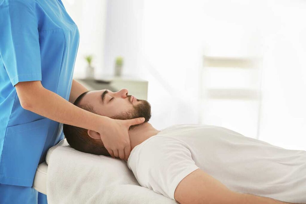A person sitting on a couch applying an ice pack to their lower back with a blanket nearby.